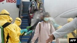 This handout photo taken and released by the Indonesian Embassy on February 2, 2020, shows officials in full protective gear disinfecting Indonesian students as they disembark upon the arrival at Hang Nadim international airport in Batam.
