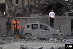 Spasioci i drugi ljudi stoje pored automobila uništenog u izralskom udaru u Rafi, na jugu Pojasa Gaze, 15. oktobra 2023.