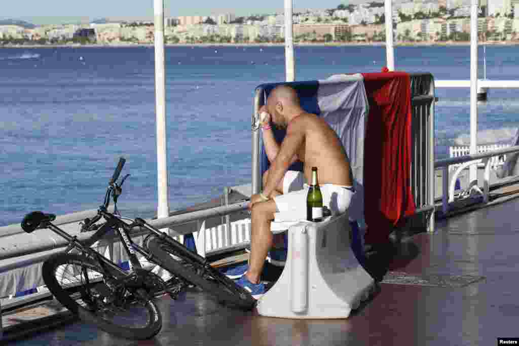 A man reacts as he sits near a French flag along the beachfront the day after a truck ran into a crowd at high speed killing scores celebrating the Bastille Day July 14 national holiday on the Promenade des Anglais in Nice, France, July 15, 2016.