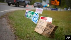 FILE - A makeshift cardboard sign leans up against campaign posters near a relief center on Oct. 3, 2024, in Vilas, N.C., in the aftermath of Hurricane Helene. 
