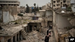 FILE - Women walk in a neighborhood heavily damaged by airstrikes in Idlib, Syria, March 12, 2020.