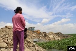 ស្ត្រី​ម្នាក់​កំពុង ​ឈរ​សម្លឹង​មើល​គ្រឿង​ចក្រ​ចាក់​ថ្ម​ចូល​បឹង​តាមោក ក្នុង​សង្កាត់​សំរោង​ត្បូង​ ​ខណ្ឌ​ព្រែកព្នៅ​ ​រាជ​ធានី​ភ្នំពេញ ថ្ងៃទី​២៧ ខែ​មិថុនា ឆ្នាំ២០២២។​ (ហាន ​ណូយ/វីអូអេ)