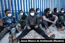 Migran duduk di luar pusat migran sementara saat melintasi pagar perbatasan di kantong Melilla, Spanyol, Afrika Utara, Spanyol 19 Januari 2021. (REUTERS/Jesus Blasco de Avellaneda)