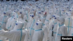 Petugas medis berbaju pelindung melambai ke arah warga Changchun saat upacara perpisahan sebelum kembali ke Meihekou, tempat mereka diberangkatkan untuk membantu mengekang wabah penyakit virus corona di Changchun, Provinsi Jilin, China 12 April 2022. (Foto: via Reuters)