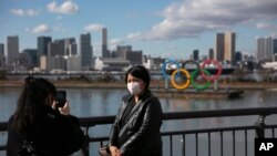 Seorang wisatawan mengenakan masker saat berfoto dengan latar belakang Cincin Olimpiade di distrik Odaiba, Tokyo, 29 Januari 2020. (Foto: dok).