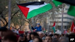 Seorang anak laki-laki melambaikan bendera Palestina di tengah aksi protes di Barcelona, Spanyol untuk mendukung rakyat Palestina dan mendesak gencatan senjata di Gaza, 20 Januari 2024. (Foto: AP Photo/Emilio Morenatt)