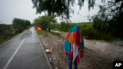 Seorang migran asal Venezuela berlindung di dalam kain saat hujan turun membasahi area tepi sungai Rio Grande di Matamoros, Meksiko, pada 13 Mei 2023. (Foto: AP/Fernando Llano)