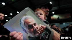 Seorang pendukung Hizbullah Lebanon menggendong seorang anak yang memegang foto mendiang komandan tertinggi Pasukan Kurdi, Qassem Soleimani, dalam pawai di pemukiman di selatan Beirut, Lebanon, 16 February 2020. (Foto: Reuters)