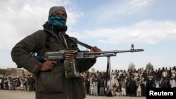 FILE - A member of the Taliban insurgent and other people stand at the site during the execution of three men in Ghazni Province, Afghanistan, April 18, 2015. 