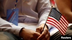 一名新公民在纽约公共图书馆的公民宣誓仪式上手持美国国旗（2018年7月3日）