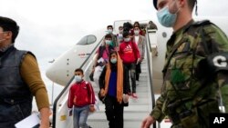 Afghan music students, faculty members and their families disembark from an airplane at Lisbon military airport, Dec. 13, 2021. 