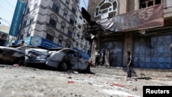 也门民众驻足观看萨那街头被毁掉的胡赛反叛武装与忠于前总统萨利赫的武装相撞的车辆。（2017年12月5日）