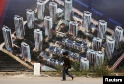 有人走过天津滨海新区一处新居民楼群的墙壁，墙上有楼群的图片（2015年10月18日）