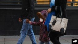 A girl wears a mask while walking with her parents in downtown Tehran, Iran, Feb. 27, 2020. Iran on Thursday closed all schools due to the coronavirus outbreak.
