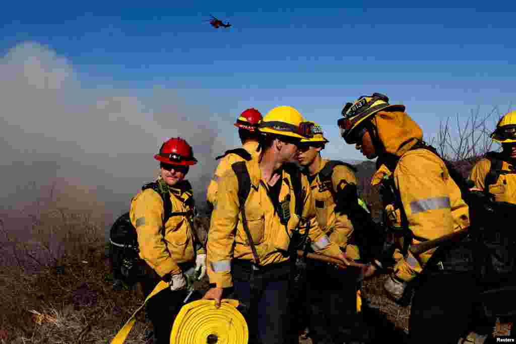 Firefighters of the Los Angeles County Fire Department gather while an helicopter flies, as the Palisades Fire rages on at the Mandeville Canyon, in Los Angeles, California, Jan. 11, 2025.