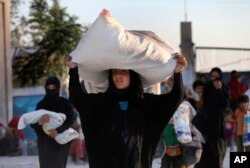 FILE - A Syrian woman who fled with her family during the battle between U.S.-backed Syrian Democratic Forces (SDF) and the Islamic State militants from Raqqa city, carries her belongings upon her arrival at a refugee camp, in Ain Issa, July 24, 2017.