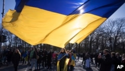 Seorang perempuan mengibarkan bendera raksasa Ukraina saat protes memperingati dua tahun invasi besar-besaran Rusia ke Ukraina, di Gerbang Brandenburg, di Berlin, Sabtu, 24 Februari 2024. (Foto: AP)