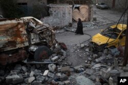 A woman walks past damaged vehicles in a neighborhood recently retaken by Iraqi security forces from Islamic State militants, in west Mosul, Iraq, April 5, 2017.