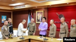 Aktor China Wang Xing berjabat tangan dengan seorang polisi Thailand di kantor polisi di distrik Mae Sot perbatasan Thailand-Myanmar, provinsi Tak, Thailand, 7 Januari 2025. (Kepolisian Kerajaan Thailand/Handout via REUTERS)