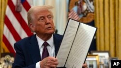 Presiden Donald Trump mengangkat instruksi presiden yang sudah ditandatangani di Ruang Oval Gedung Putih, di Washington, 23 Januari 2025. (Foto: AP)