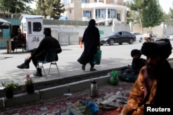 Seorang perempuan Afghanistan berjalan melintas sejumlah tentara Taliban di pos pemeriksaan di Kabul, Afghanistan, 6 Juli 2023. (Foto: Ali Khara/Reuters)