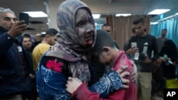 Seorang perempuan Palestina yang terluka, menggendong putranya yang juga mengalami luka-luka, dalam pemboman Israel di Jalur Gaza, menunggu perawatan di rumah sakit di Deir al Balah, Jalu Gaza, Jumat 8 Desember 2023.