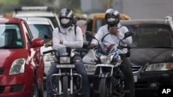 Pengendara sepeda motor mengenakan masker di jalanan yang penuh polusi di New Delhi, India.Polusi udara di India