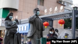 资料照片：中国武汉市，一名女子正走过带着口罩的雕塑面前。期间，世卫组织新冠溯源专家小组正在武汉考察。（2021年1月29日）