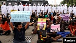 Polisi mengenakan APD berbaris di dekat aktivis Papua yang berunjuk rasa di luar Kompleks Monumen Nasional di Jakarta, Indonesia, 1 Desember 2021. (REUTERS/Willy Kurniawan).