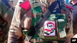 FILE - A Syrian soldier, with a picture of now former Syrian President Bashar Assad on his military uniform, organizes crowds during the opening ceremony of the crossing between the Iraqi and Syria, Sept. 30, 2019.