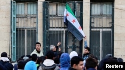 Seorang guru mengibarkan bendera penguasa baru Suriah di sekolah yang dibuka kembali setelah penggulingan Bashar al-Assad, Damaskus, 15 Desember 2024. (Reuters)