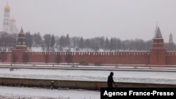 FILE - A pedestrian walks along an embankment of the Moskva river with the Kremlin on the background during a snowfall in Moscow, Jan. 21, 2022. 