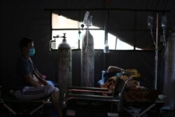 Seorang pasien COVID-19 duduk di atas velbed di tenda sementara di luar ruang gawat darurat rumah sakit pemerintah di Bekasi, 25 Juni 2021. (Foto: REUTERS/Willy Kurniawan)