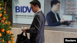 FILE - A man counts money he withdrew from an ATM machine at the headquarters of the Bank for Investment and Development of Vietnam in Hanoi.