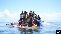 Pengungsi Rohingya berdiri di atas badan kapal mereka yang terbalik di perairan Aceh Barat, Kamis, 21 Maret 2024. (Foto: Reza Saifullah/AP Photo)