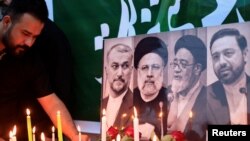 Seorang pria tampak menyalakan lilin di dekat foto mendiang Presiden Iran Ebrahim Raisi dan sejumlah tokoh lainnya di luar kedutaan besar Iran di Baghdad, Irak, pada 20 Mei 2024. (Foto: Reuters/Thaier Al-Sudani)