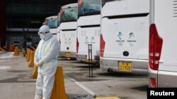 2022北京冬奥会一位身穿防护服的工作人员，他身后是专门接送冬奥会人员的大巴士。
