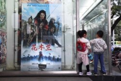 Children play next to a poster of the Disney movie "Mulan" outside a cinema in Beijing on September 11, 2020.