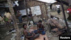 FILE - Rohingya people pass their time in a damaged shelter in Rohingya IDP camp outside Sittwe, Rakhine state, Aug. 4, 2015. Kerry noted the Rohingya as a group that has been 'singled out' for discrimination.