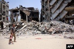 Seorang pria Palestina menggandeng tangan seorang anak kecil saat mereka berjalan melewati reruntuhan bangunan di kamp pengungsi Jabalia, di Jalur Gaza utara pada 3 Juni 2024. (Foto: AFP)