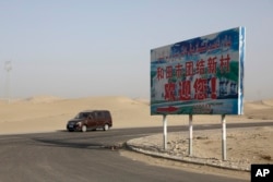 FILE - A car drives by a sign reading "Welcome to the Hotan Unity New Village" in China's Xinjiang region on Sept. 21, 2018. Authorities have been changing the names of villages inhabited by Uyghurs to reflect the ruling Communist Party's ideology.