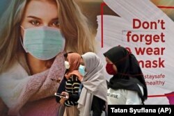 Wanita bermasker melewati iklan yang mempromosikan kesadaran akan wabah virus corona di sebuah pusat perbelanjaan di Jakarta, Rabu, 1 Juli 2020. (Foto: AP/Tatan Syuflana)