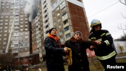 Vatrogasci pomažu ženi koja je napustila soliter pogođen u ruskom raketnom udaru, u Kijevu, 7. febraura 2024.