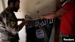 Anggota Pasukan Demokratik Suriah memegang bendera militan ISIS yang ditemukan di sebuah gedung di sebelah stadion di Raqqa, Suriah, 4 Oktober 2017. (Foto: REUTERS/Erik De Castro)