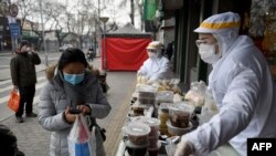 北京一家餐馆的工作人员2月20日身穿防护服在餐馆外出售食品。
