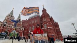 Pristalica ruskog predsednika Vladimira Putin deli novine na prvu godišnjicu ruske vojne kampanje u Ukrajini. Na panou piše -"On i ja smo za suverenitet Rusije. A vi?"