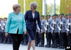 German Chancellor Angela Merkel, left, and British Prime Minister Theresa May walk on the red carpet during a military welcoming ceremony at the chancellery in Berlin, July 20, 2016.
