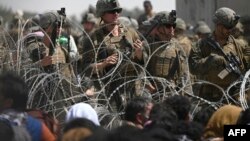 Para tentar AS berjaga di balik kawat berduri, sementara warga Afghan duduk di pinggir jalan dekat kawasan militer Bandara Internasional Kabul, 20 Agustus 2021.