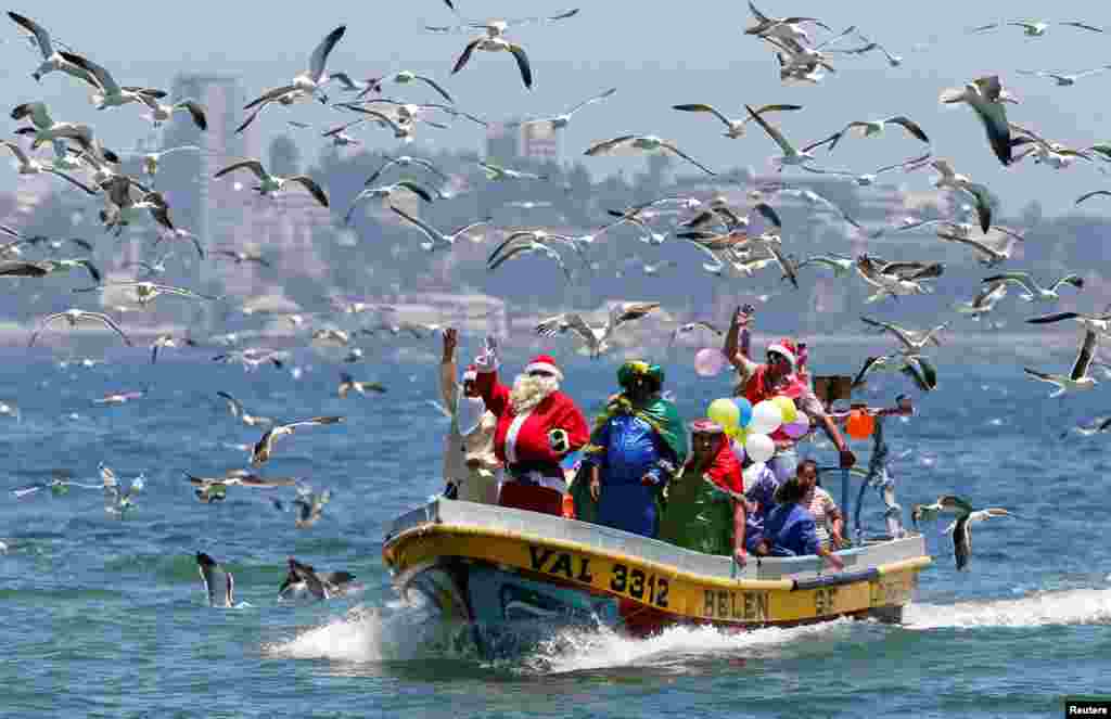 2017年12月24日,圣诞节前夕,智利瓦尔帕莱索海岸附近,一位穿着圣诞老人服装的男子在渔夫的船上挥手致意。