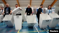 Petugas pemilu menunjukkan kotak suara kosong sebelum pelaksanaan pemungutan suara pertama untuk pemilihan anggota parlemen di Godthaabshallen, Nuuk, Greenland, 11 Maret 2025. (Ritzau Scanpix/Mads Claus Rasmussen via Reuters)